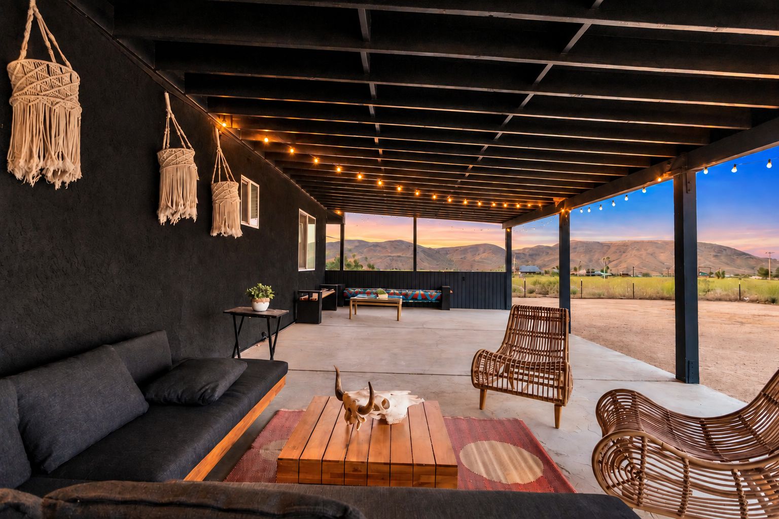 An outdoor patio with a black sofa, wicker chairs, a wooden coffee table, and macramé wall hangings.