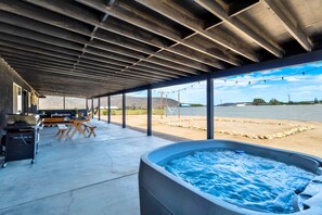 Een overdekt buitengebied met een jacuzzi, picknicktafels en een barbecue.