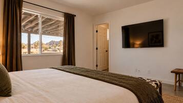 Una camera da letto con un letto, una televisione a muro e vista sull'esterno attraverso una finestra.