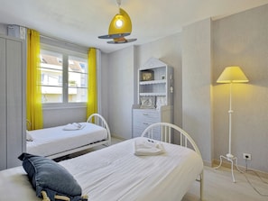 Ein Schlafzimmer mit zwei Betten, einem Nachttisch, einer Lampe, einem Kleiderschrank und einem Fenster mit Vorhängen.
