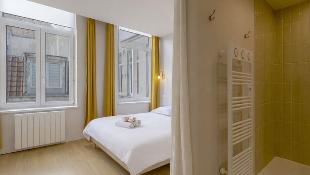 Ein Schlafzimmer mit Bett, Heizkörper, Fenster und einem Badezimmer mit Handtuchhalter.