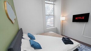 Hotellihuone, jossa on sänky, seinälle asennettu televisio, ikkuna ja lamppu.