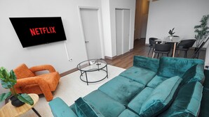 Moderni olohuone, jossa on turkoosi sohva, oranssi nojatuoli ja televisio, jonka näytöllä näkyy teksti ”NETFLIX”.