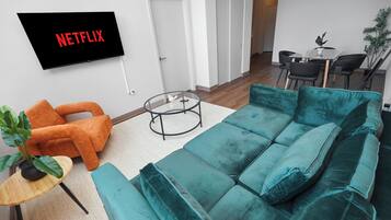 Una sala de estar moderna con un sofá color turquesa, un sillón naranja y un televisor que muestra 'NETFLIX'.