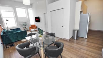Un espacio de oficina moderno con una mesa de vidrio, sillas negras, un sofá verde, una puerta blanca y un refrigerador.