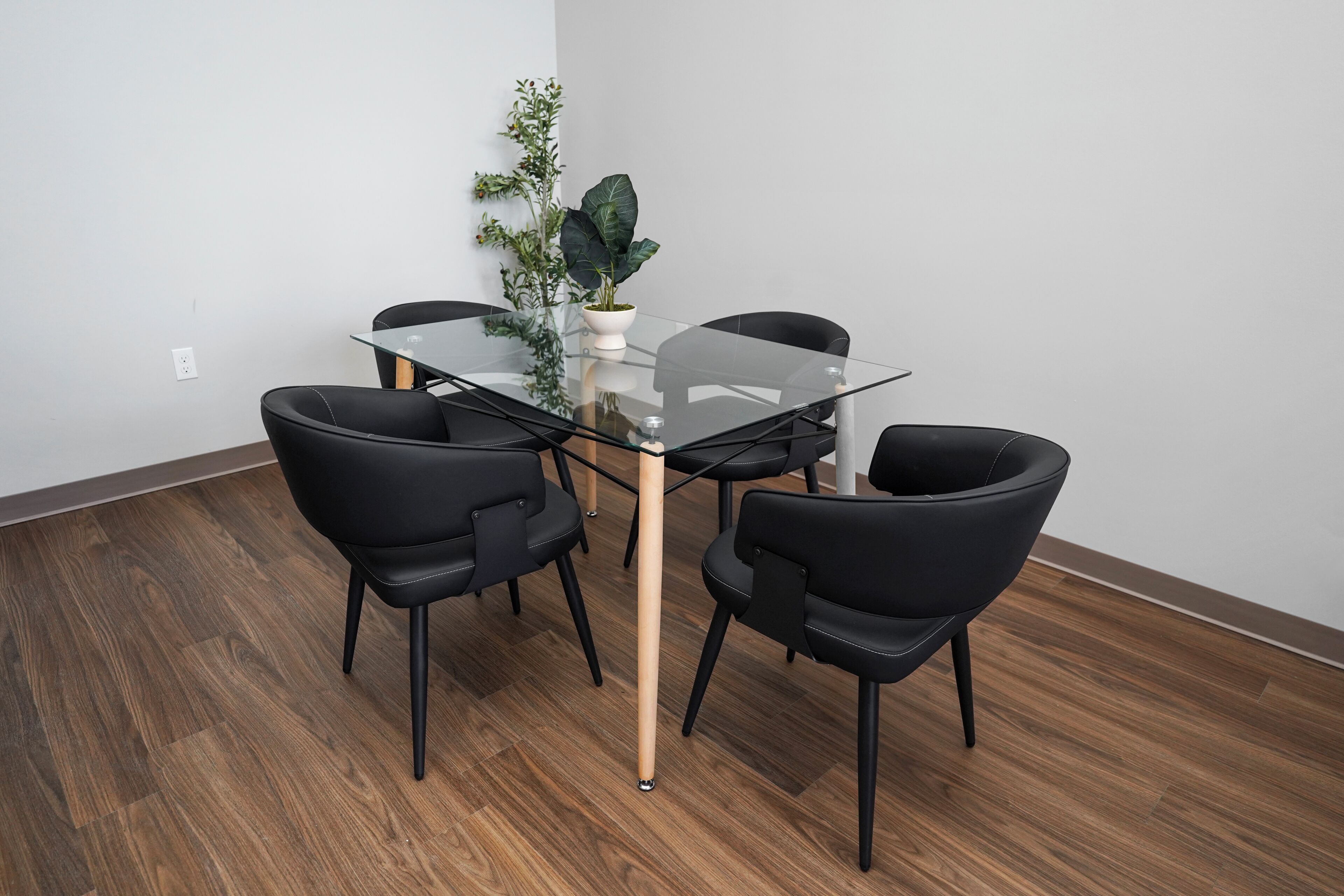Un comedor moderno con una mesa de vidrio, sillas negras y una planta en maceta.