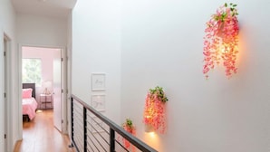 A hallway with a staircase, a bed with pink bedding, and wall-mounted light fixtures with hanging plants. - Pink Longhorn + Glam Getaway + Walk to UT  Downtown Pink Longhorn (Austin)