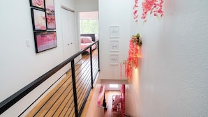 A staircase with a wooden handrail and a white wall with framed pictures and decorative flowers. - Pink Longhorn + Glam Getaway + Walk to UT  Downtown Pink Longhorn (Austin)