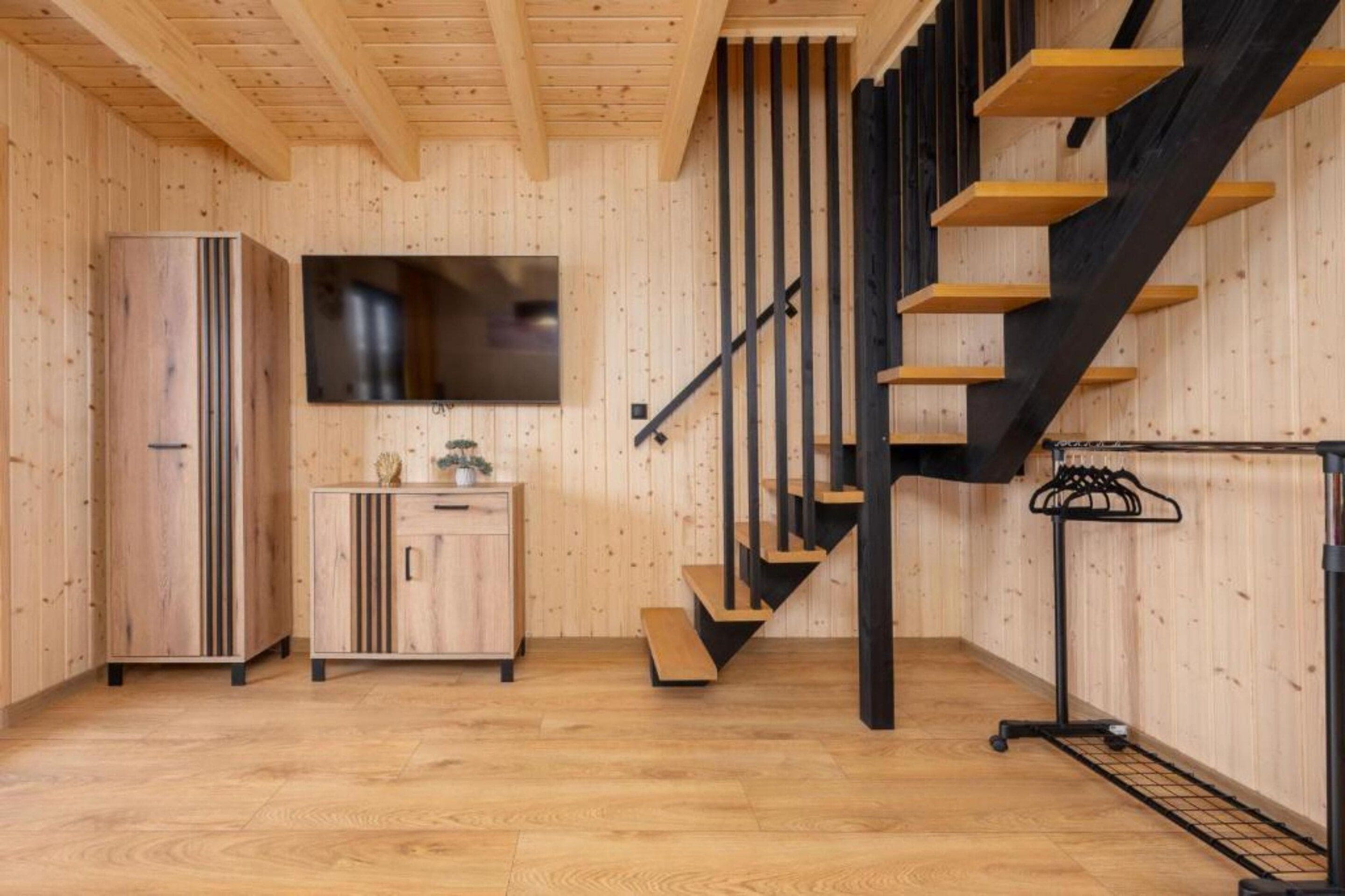 Interior de madera con una zona de cocina, una escalera de madera y un televisor montado.