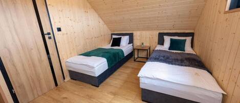 A small, wooden-paneled room with two beds, each with a pillow and a blanket.