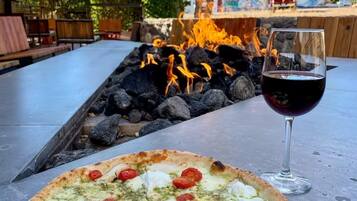 Eine Pizza mit Belag und ein Glas Rotwein auf einem Tisch im Freien.
