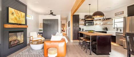 A modern living room with a fireplace, seating area, and a kitchen with a bar.