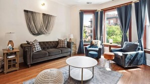 A living room with a sofa, armchairs, a round coffee table, and a view of the city through large windows. - Chicago Gem: Wrigley - Lakefront - Red Line Train (Chicago)