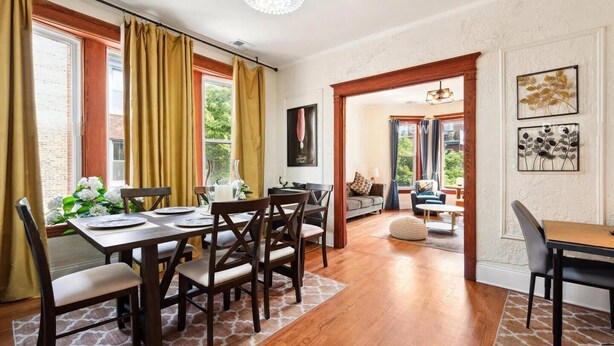 A dining area with a wooden table and chairs, a chandelier, and a view of the outdoors. - Chicago Gem: Wrigley - Lakefront - Red Line Train (Chicago)
