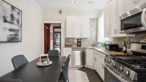 A modern kitchen with stainless steel appliances, a dining area with a table and chairs, and a hallway leading to another room. - Chicago Gem: Wrigley - Lakefront - Red Line Train (Chicago)