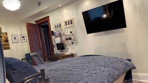A bedroom with a bed, a desk, a chair, a TV, and a wall-mounted shelf with pictures. - Chicago Gem: Wrigley - Lakefront - Red Line Train (Chicago)