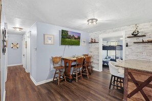 Ein Essbereich mit Holztisch und Stühlen, einem an der Wand montierten Fernseher und einer rustikalen Küche mit Arbeitsplatte aus Holz.
