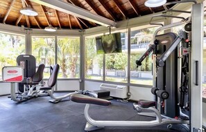 Ein Fitnessstudio mit Trainingsgeräten, großen Fenstern und einem Fernsehbildschirm.