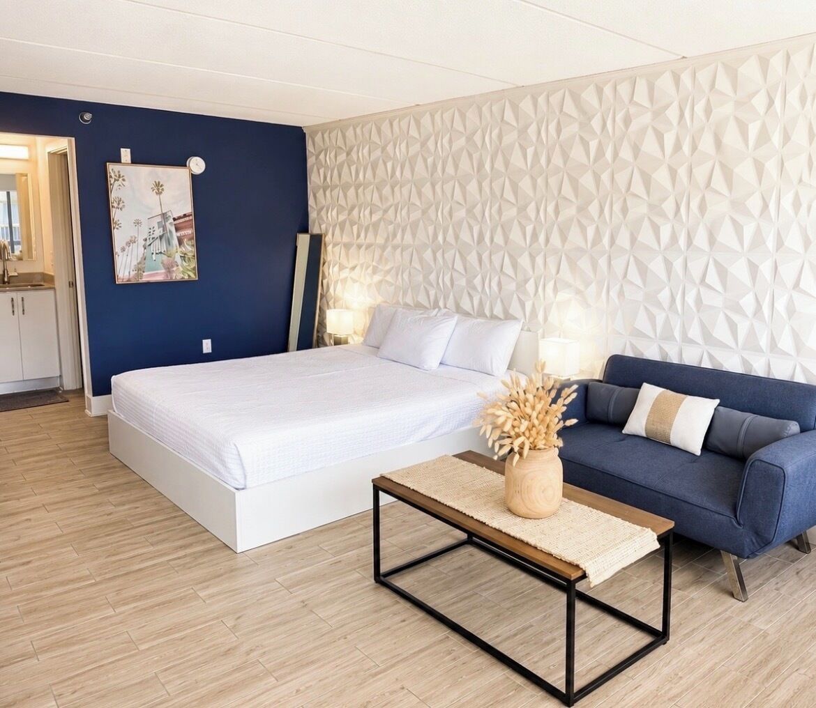 A bedroom with a bed, a sofa, a coffee table, and a wall with a geometric pattern.