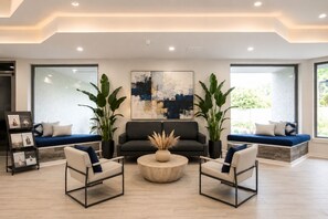 Ein modernes Wohnzimmer mit einer Couch, zwei Sesseln, einem Couchtisch und großen Fenstern.