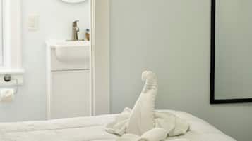 A bedroom with a bed, a folded towel, a wall-mounted TV, and a bathroom visible through an open door.