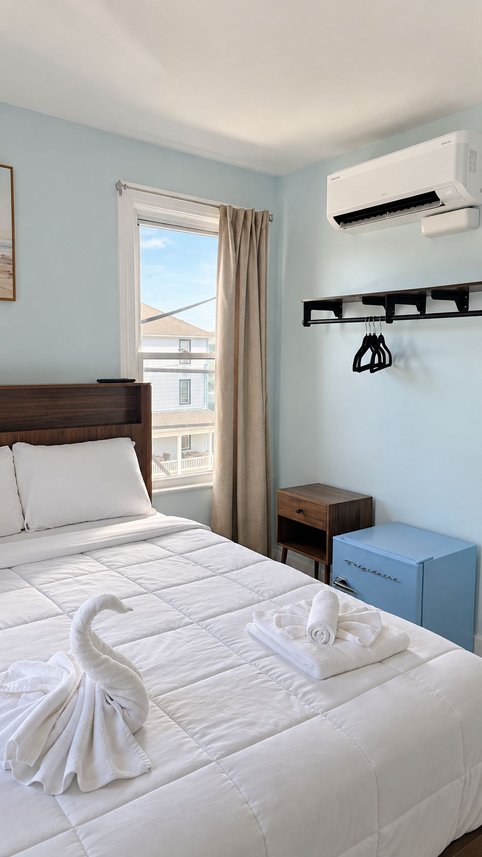 Una habitación de hotel con una cama, un ventanal, aire acondicionado, un escritorio pequeño y un armario azul.
