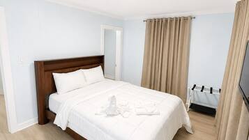 A hotel room with a bed, a TV, and a window with curtains.