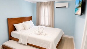 Un dormitorio con cama de madera, un banco, una lámpara en el techo, un equipo de aire acondicionado y un televisor montado en la pared.