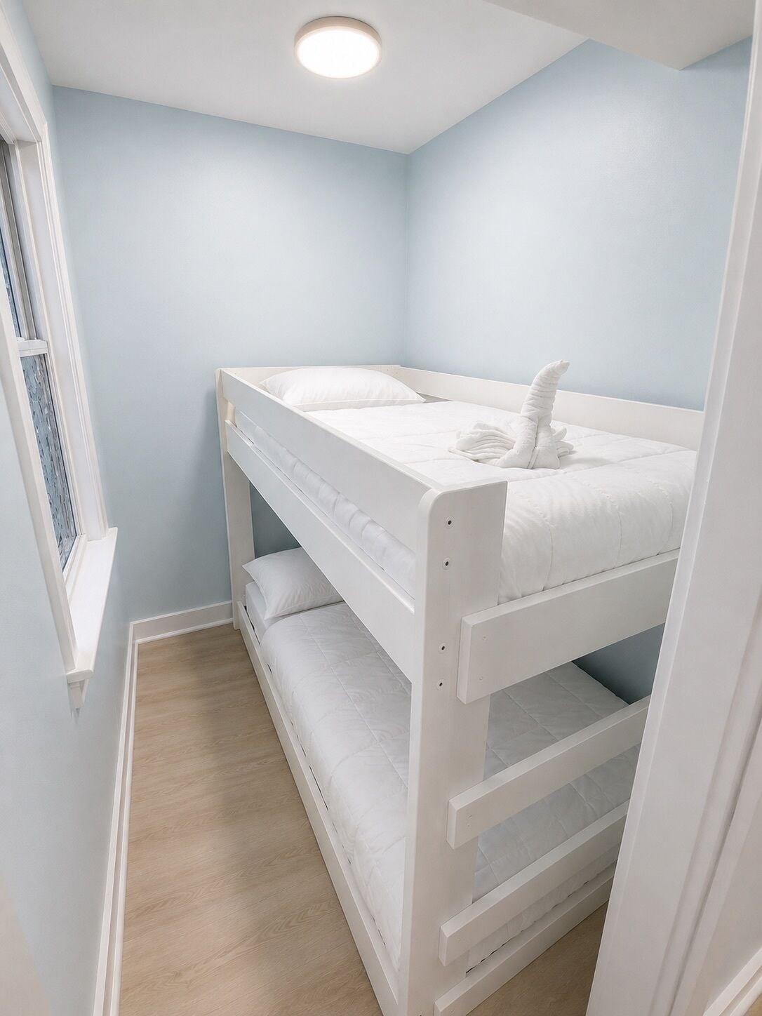 Camera con letto a castello, una finestra, pareti azzurro chiaro e pavimento in legno.