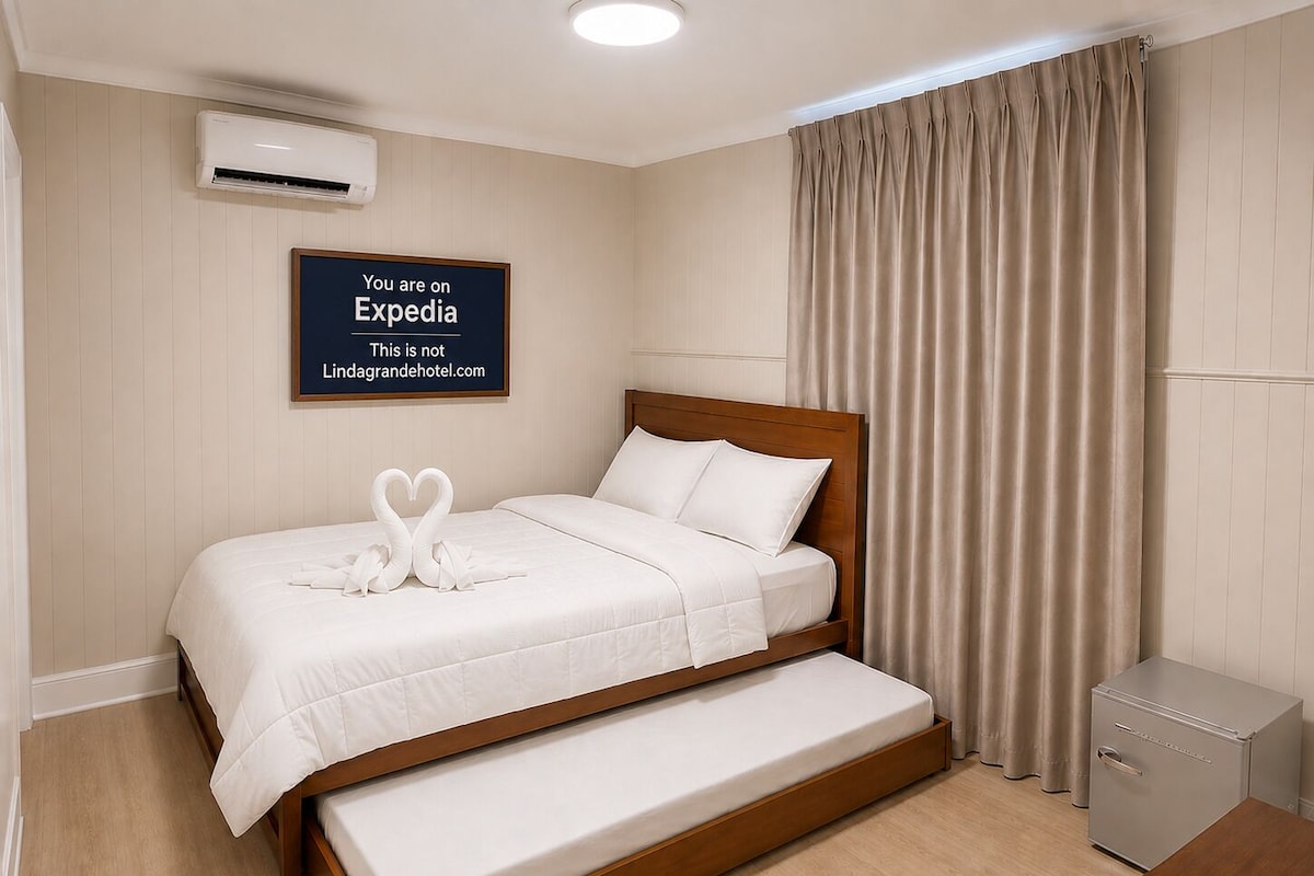 A hotel room with a bed, a bench, an air conditioning unit, a desk, and a wardrobe.
