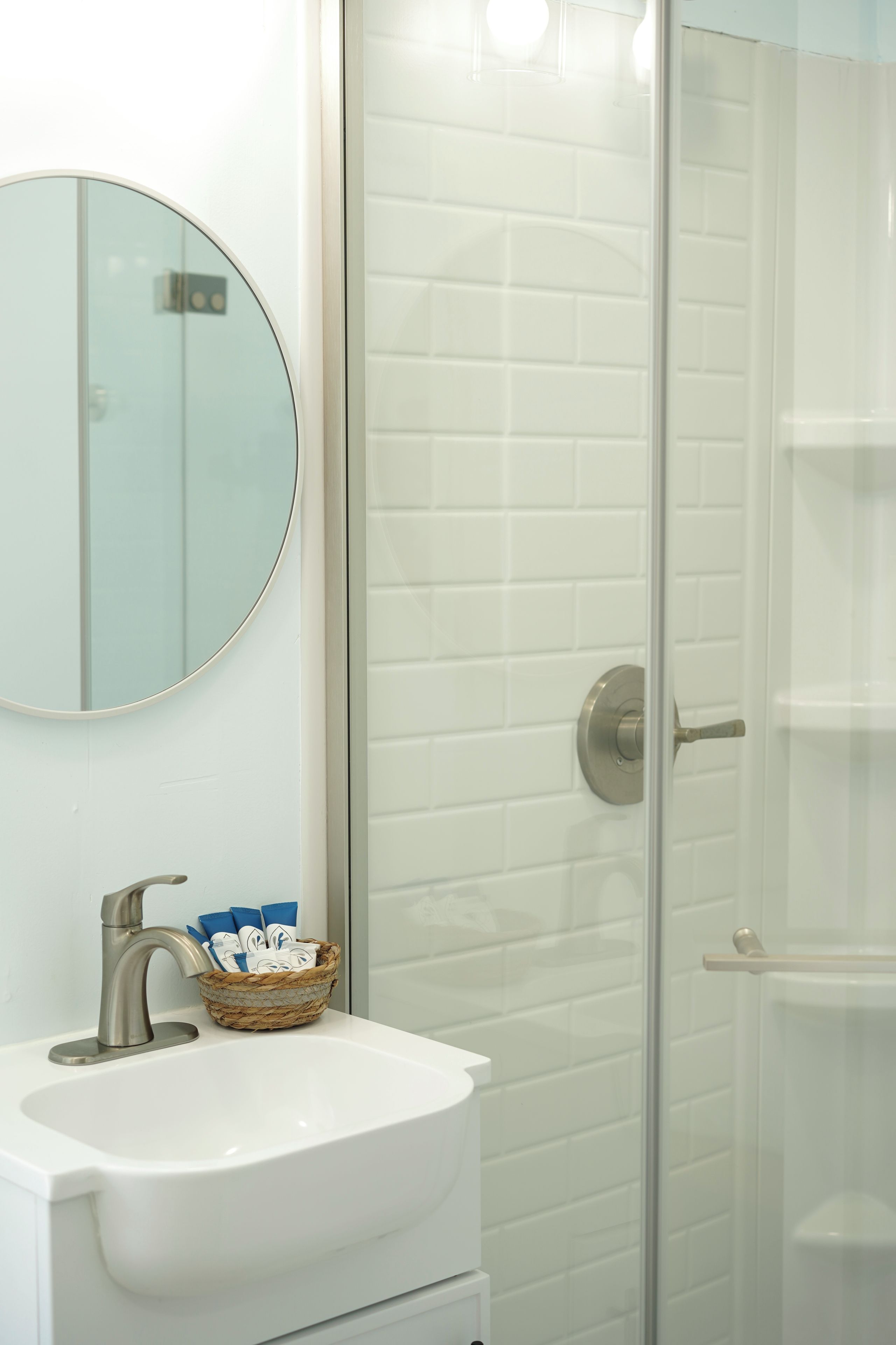 A bathroom with a white sink, a round mirror, and a glass shower enclosure.