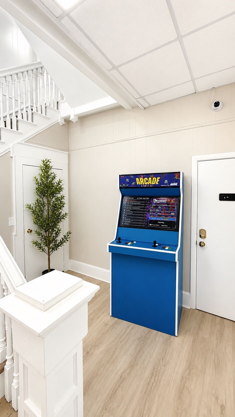 A room with a white staircase, a door, and a blue arcade machine.