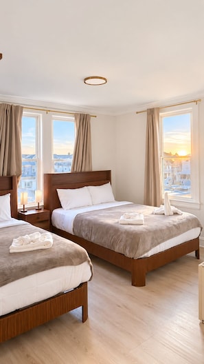A hotel room with two beds, a wooden headboard, a nightstand with a lamp, and a view of the city through large windows.