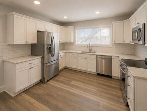 A kitchen with white cabinets, a stainless steel refrigerator, a dishwasher, and a microwave. - The Linda Grande Hotel (Ocean City)