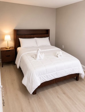A neatly made bed with a wooden headboard, a bedside lamp, and a swan-shaped towel decoration. - The Linda Grande Hotel (Ocean City)