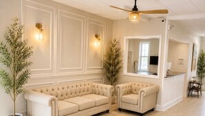 Un salón espacioso con dos sofás color beige, un ventilador de techo de madera y un espejo grande que refleja la habitación.
