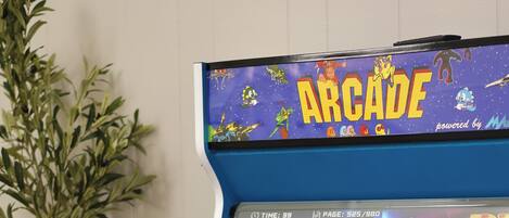 Una máquina recreativa azul con una pantalla mostrando un menú de juego, rodeada de una planta.