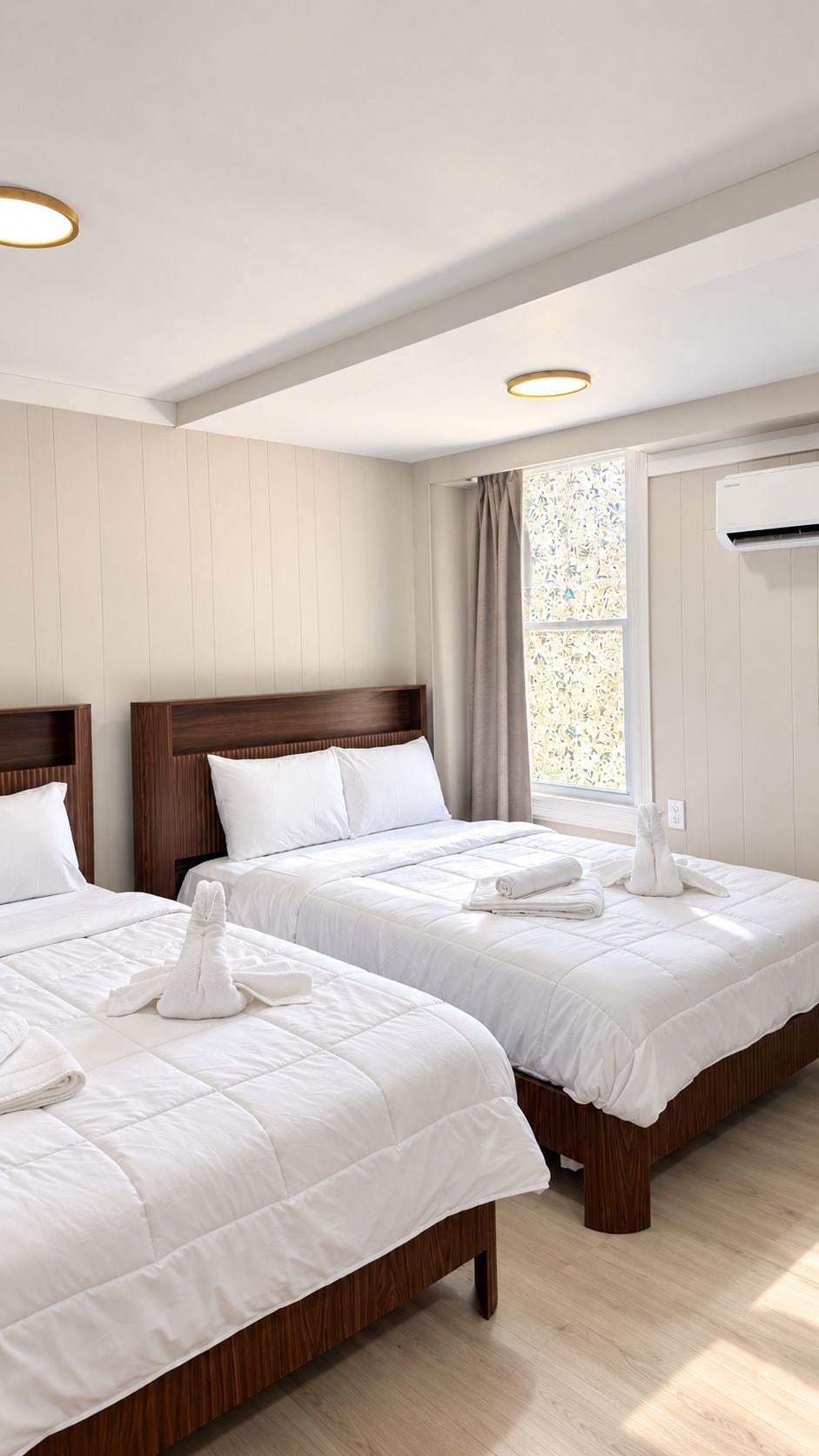 A hotel room with two beds, a window with a view, and an air conditioning unit.