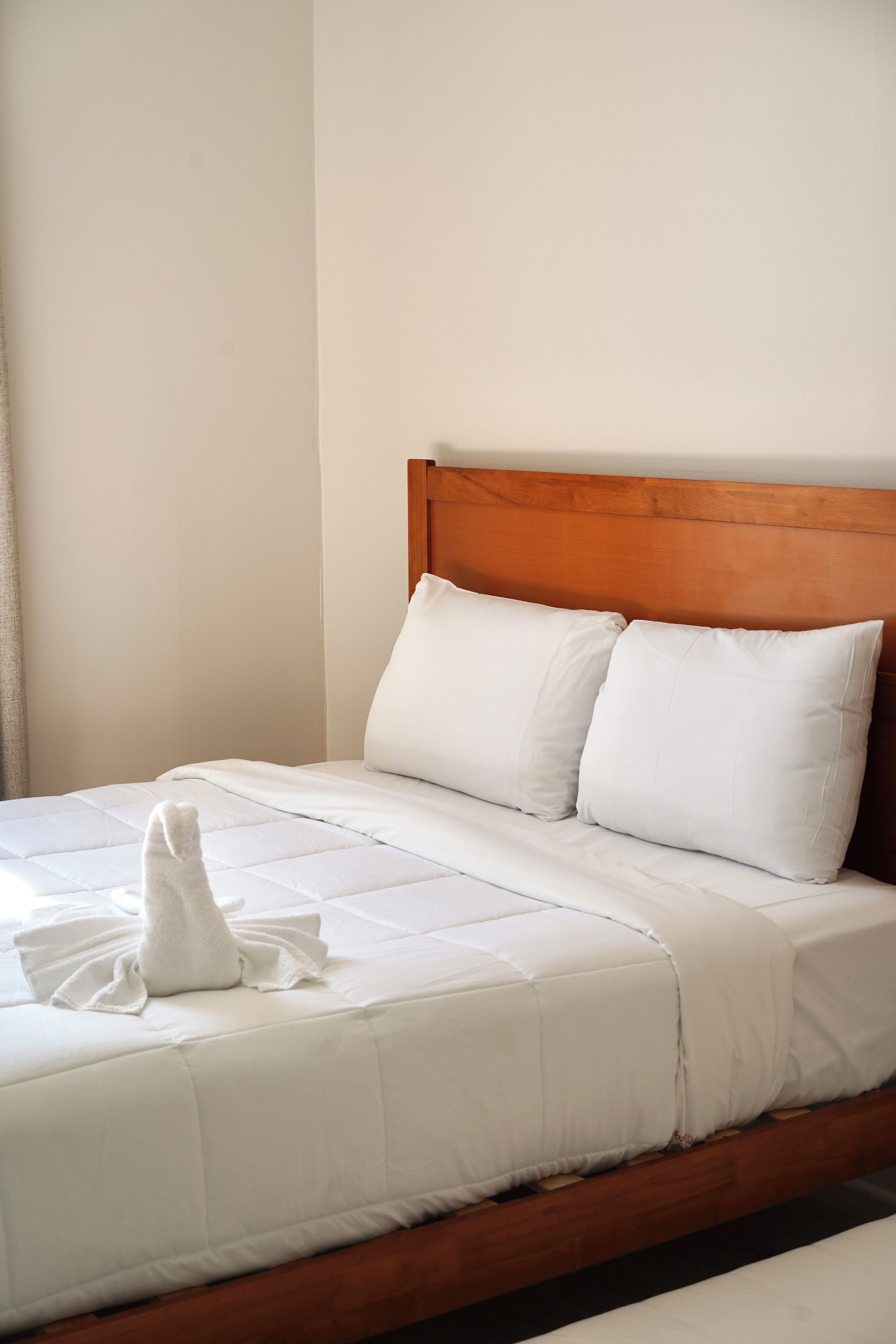Una cama bien hecha con sábanas y almohadas blancas, un cabecero de madera y una toalla blanca sobre la cama.