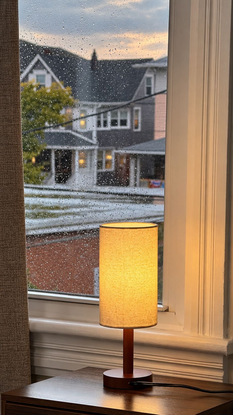 Una lámpara sobre una mesa cerca de una ventana con gotas de lluvia en el vidrio.