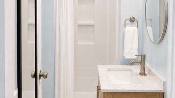 A bathroom with a shower, a sink, a mirror, and a door.