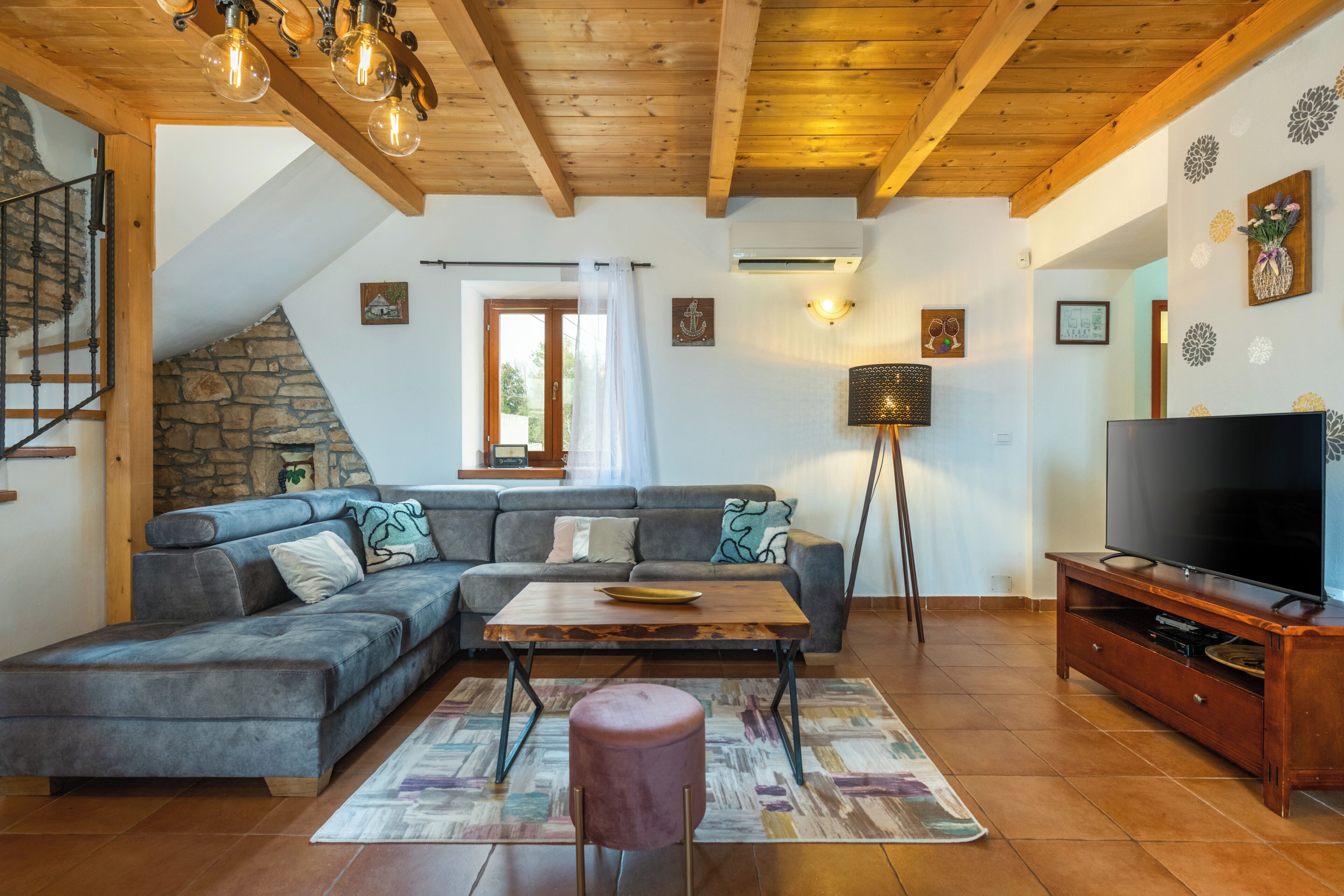 Ein Wohnzimmer mit Ecksofa, Couchtisch aus Holz, Fernseher und Kamin aus Stein.