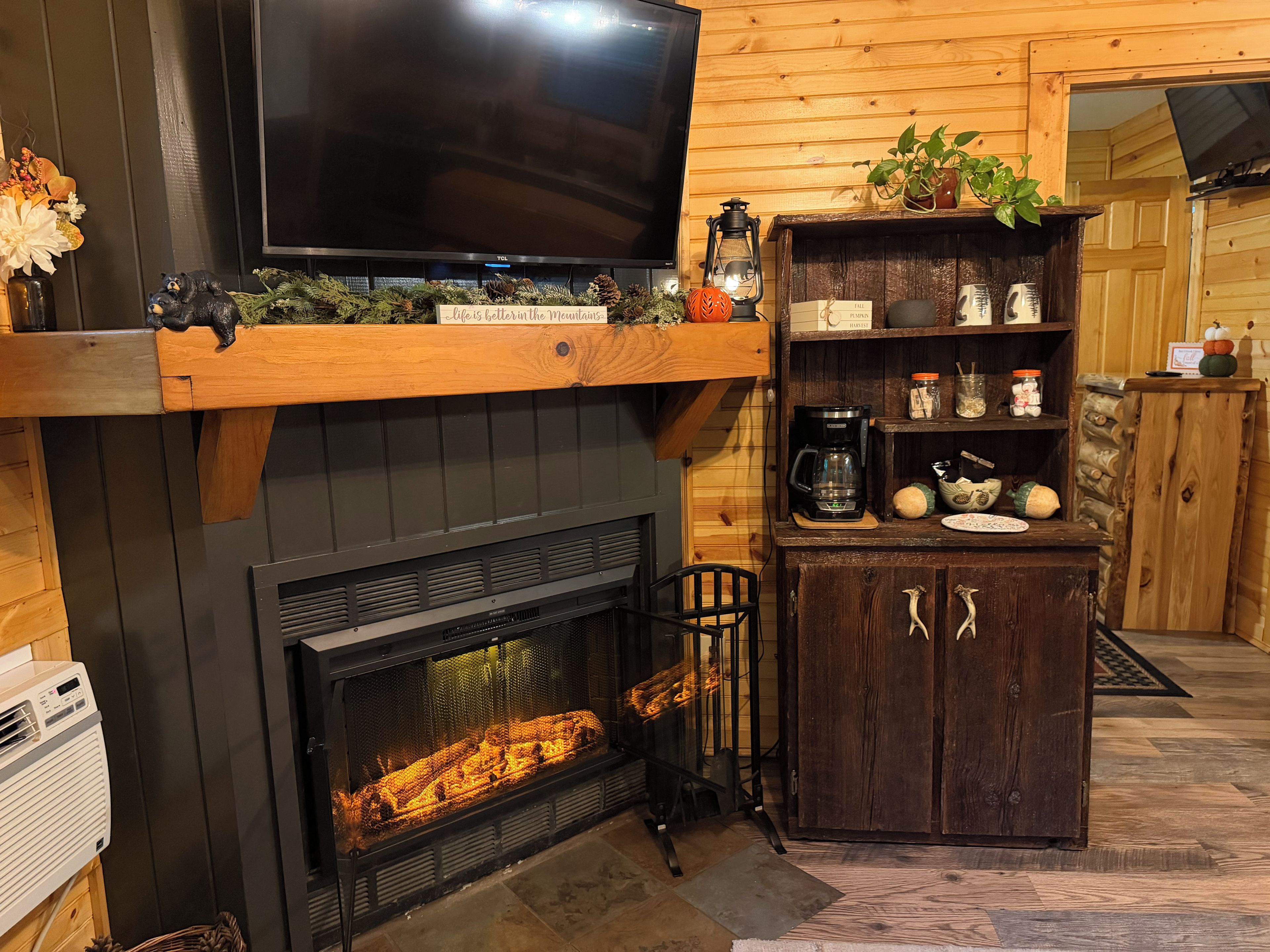 Una sala de estar acogedora con chimenea, un televisor montado encima y un estante de madera con objetos decorativos.