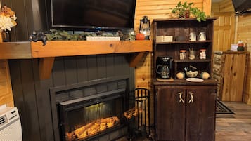 Una sala de estar acogedora con chimenea, un televisor montado encima y un estante de madera con objetos decorativos.