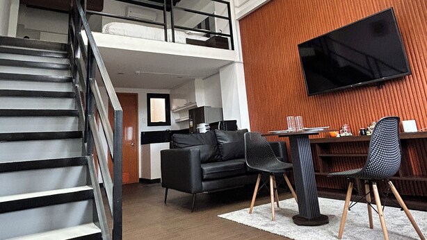 A modern interior with a staircase, a dining area, a sofa, and a TV mounted on a wooden wall.