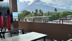 A covered outdoor seating area with tables and chairs, overlooking a mountain and a body of water.