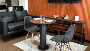 A modern living room with a sofa, two chairs, a round table, a flat-screen TV, and a wooden wall panel.