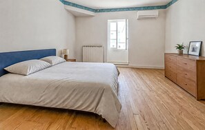Ein Schlafzimmer mit Bett, Holzboden, Schminktisch, Heizkörper, Fenster und Klimaanlage.