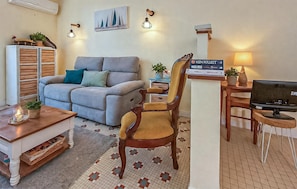 Ein Wohnzimmer mit einer Couch, einem Holzstuhl, einem Fernseher, einer Lampe, einem kleinen Tisch mit einer Pflanze und einem Schild an der Wand.
