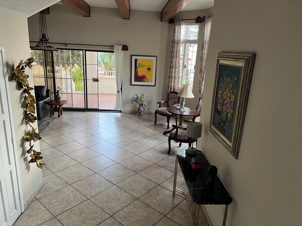 A spacious living area with a tiled floor, a dining table with chairs, a sofa, a lamp, and a painting on the wall.